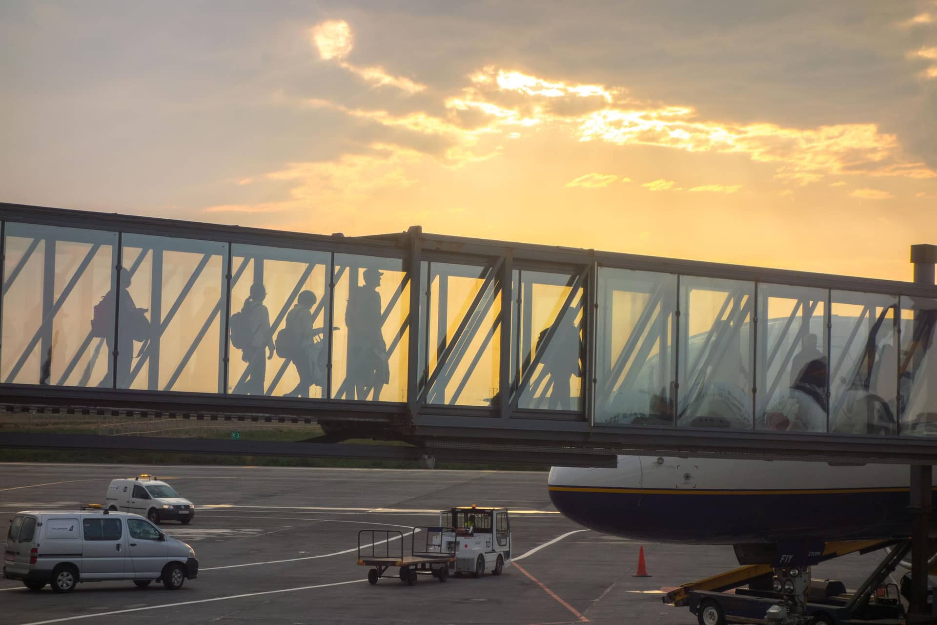 Travelers walking through a glass airport jet bridge